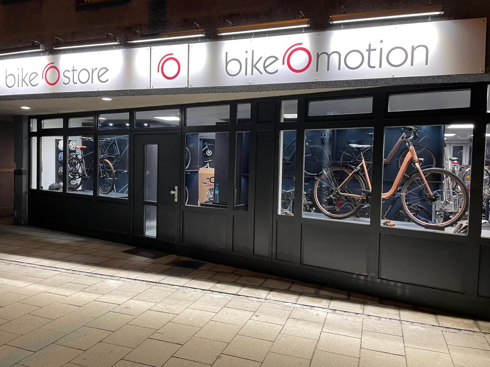 Ladenfront von bikeOstore und bikeOmotion am Abend, beleuchtete Schilder, Räder im Schaufenster