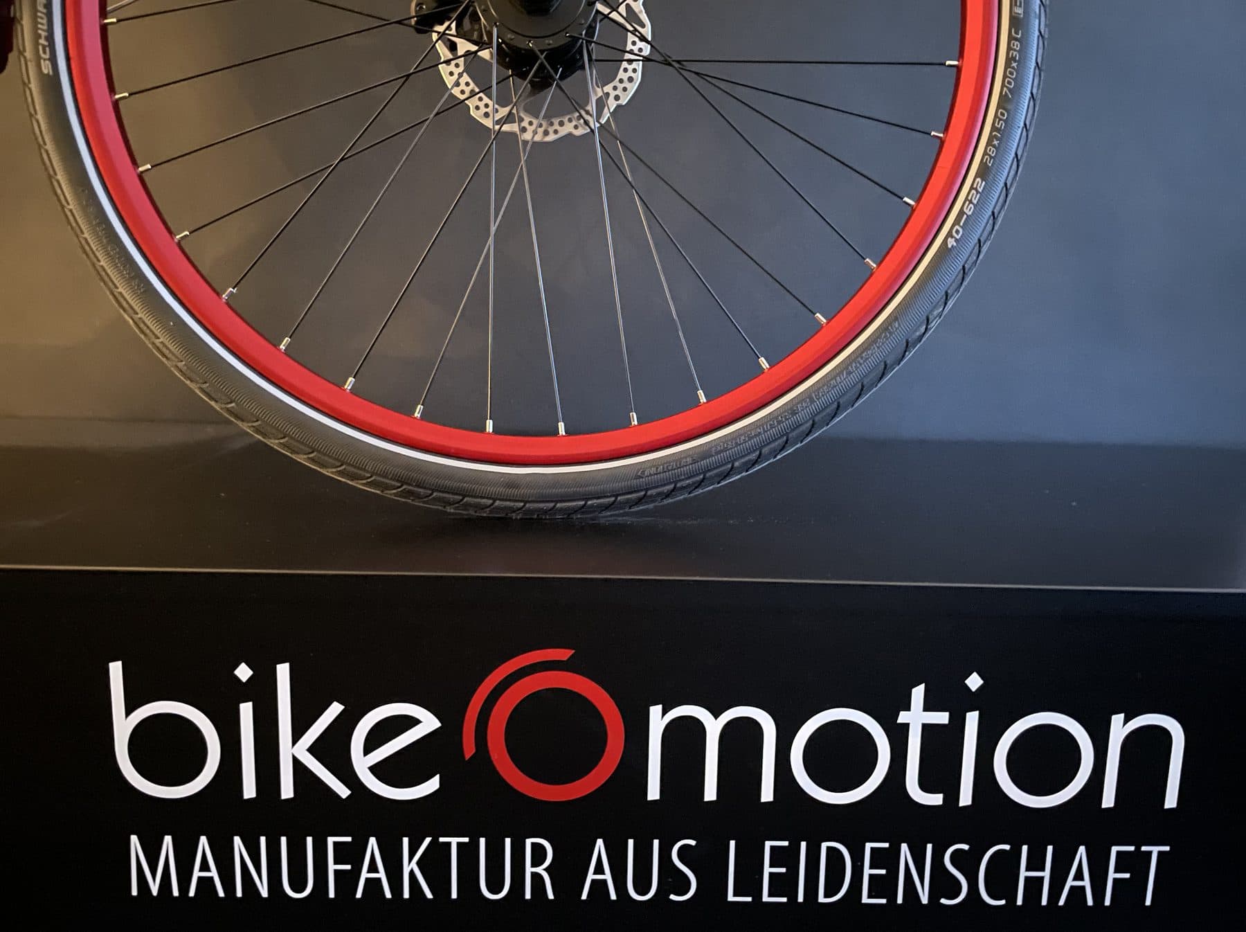 Laufrad vor dem Schild bikeOmotion, Manufaktur aus Leidenschaft